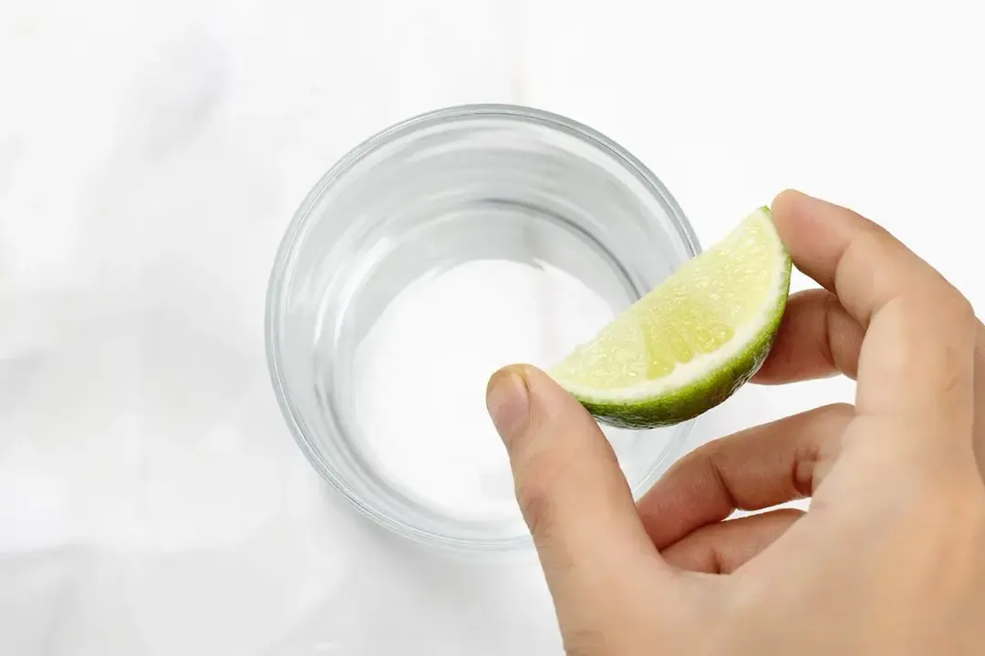 Holding a lime wedge over a short glass