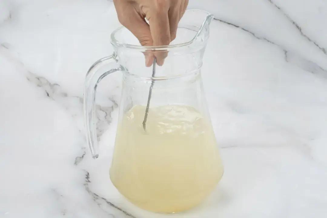 A spoon stirring lemonade in a clear pitcher