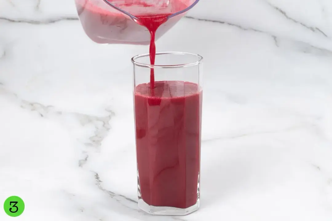 A pitcher of beetroot juice pouring into a tall clear glass