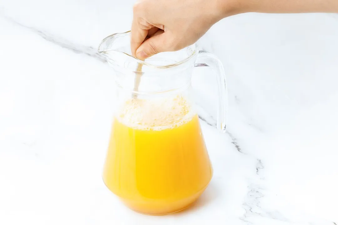 a hand holding a spoon to stir juice in a pitcher
