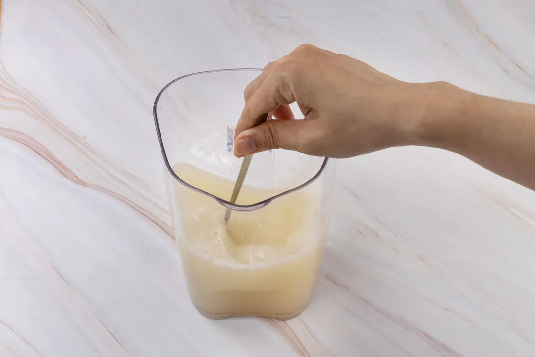 a hand holding a spoon to stir a juice pitcher