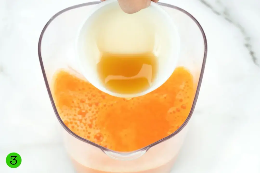 Pouring honey from a bowl into a clear pitcher of orange juice