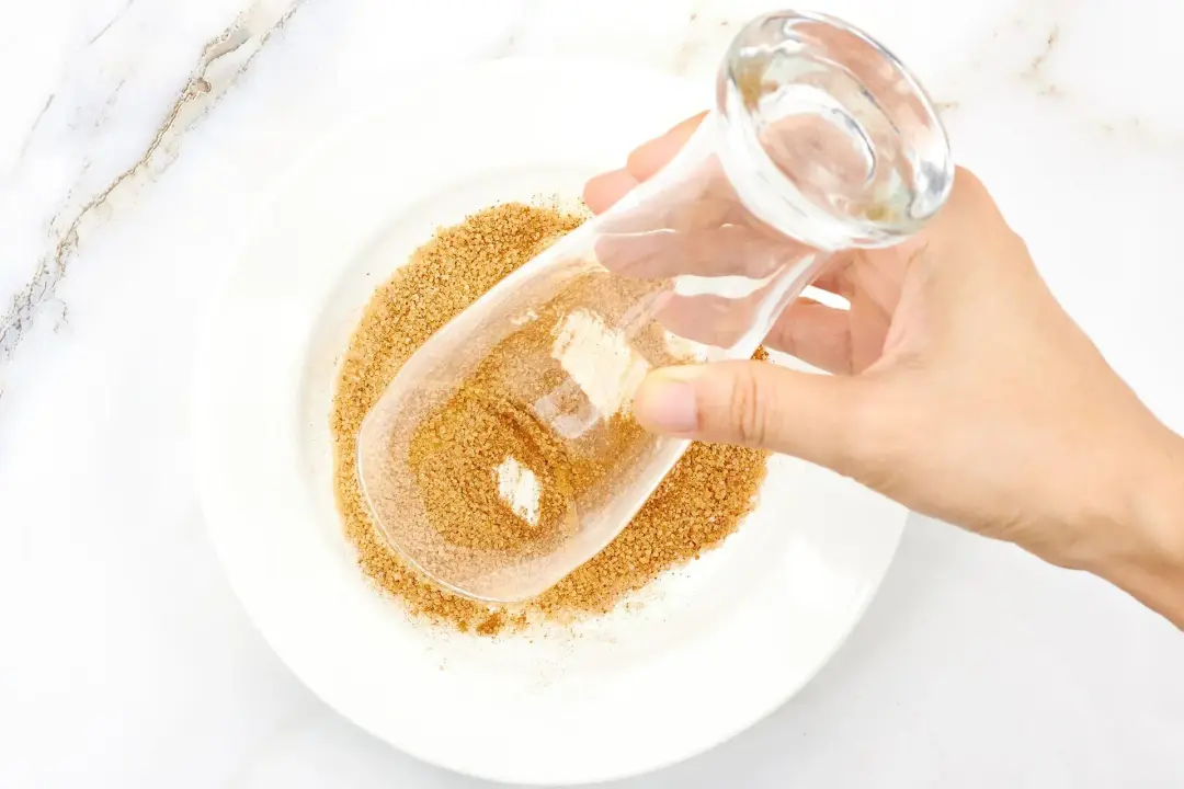 A hand dipping a clear glass into a plate of brown sugar