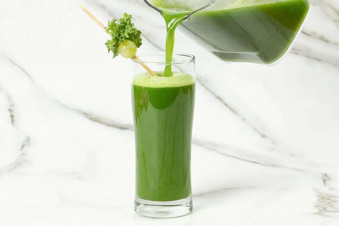 A glass of green machine juice being poured out of the pitcher