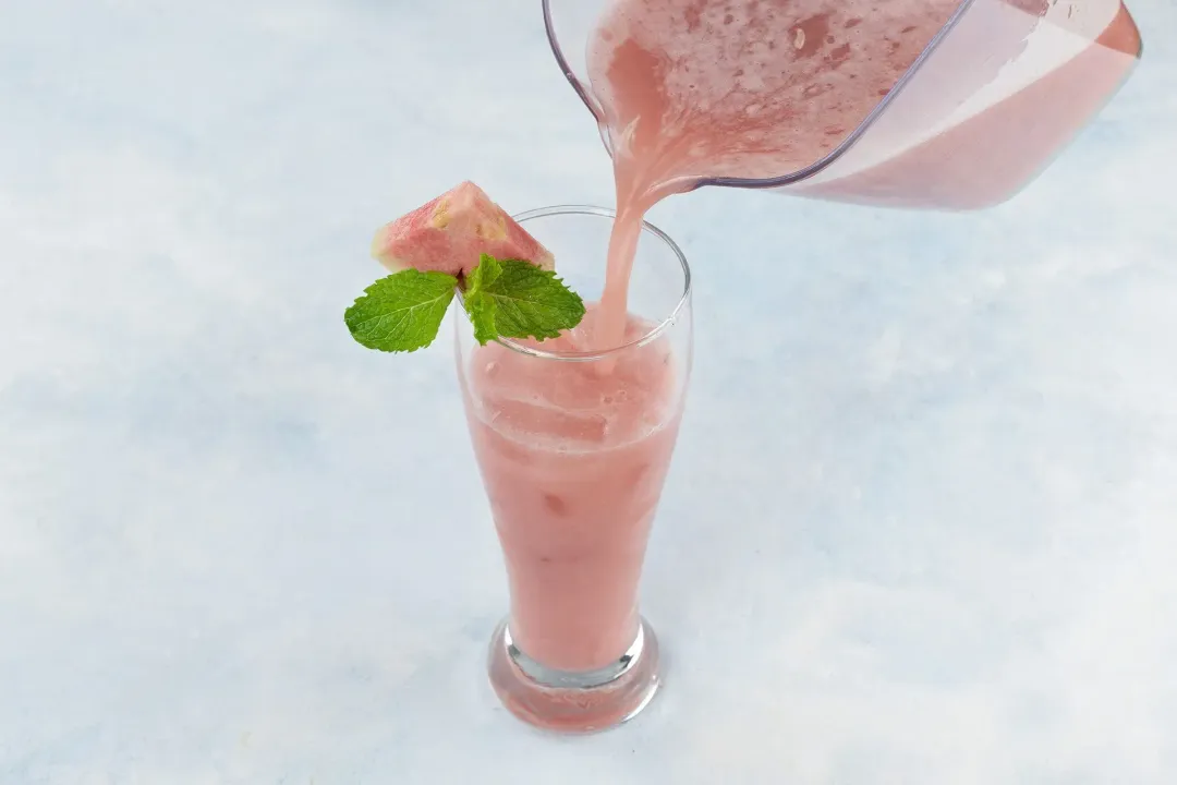 Guava juice being poured into a tall glass from a large juice container