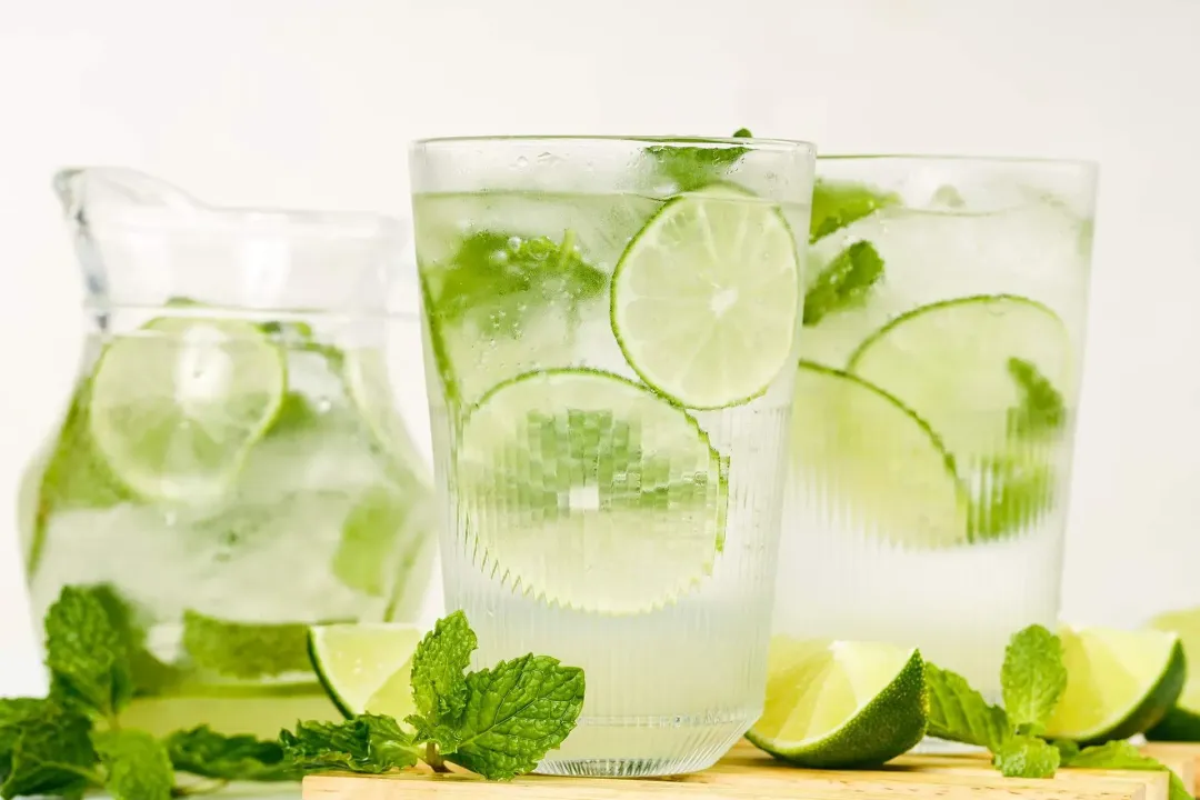 Three mojitos glasses put side by side, with lime wedges and baby mints lying around