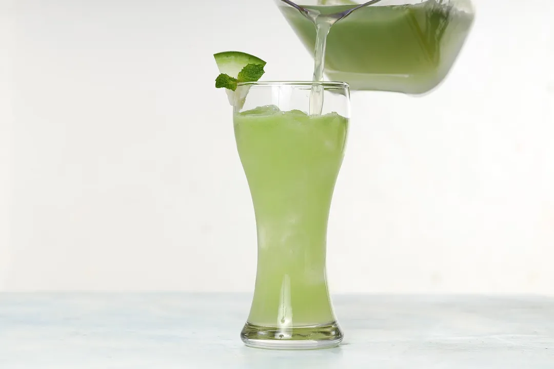 A jug pouring winter melon juice into a tall glass.