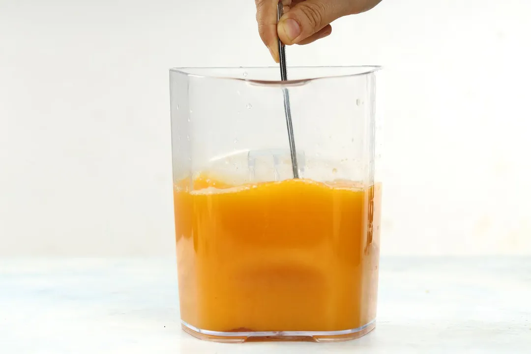 hand holds a spoon on a pitcher of orange liquid