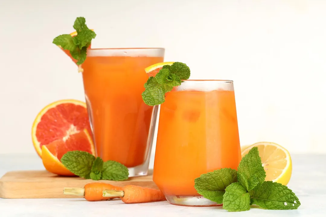 front shot of two glasses of grapefruit carrot juice on a wooden tray