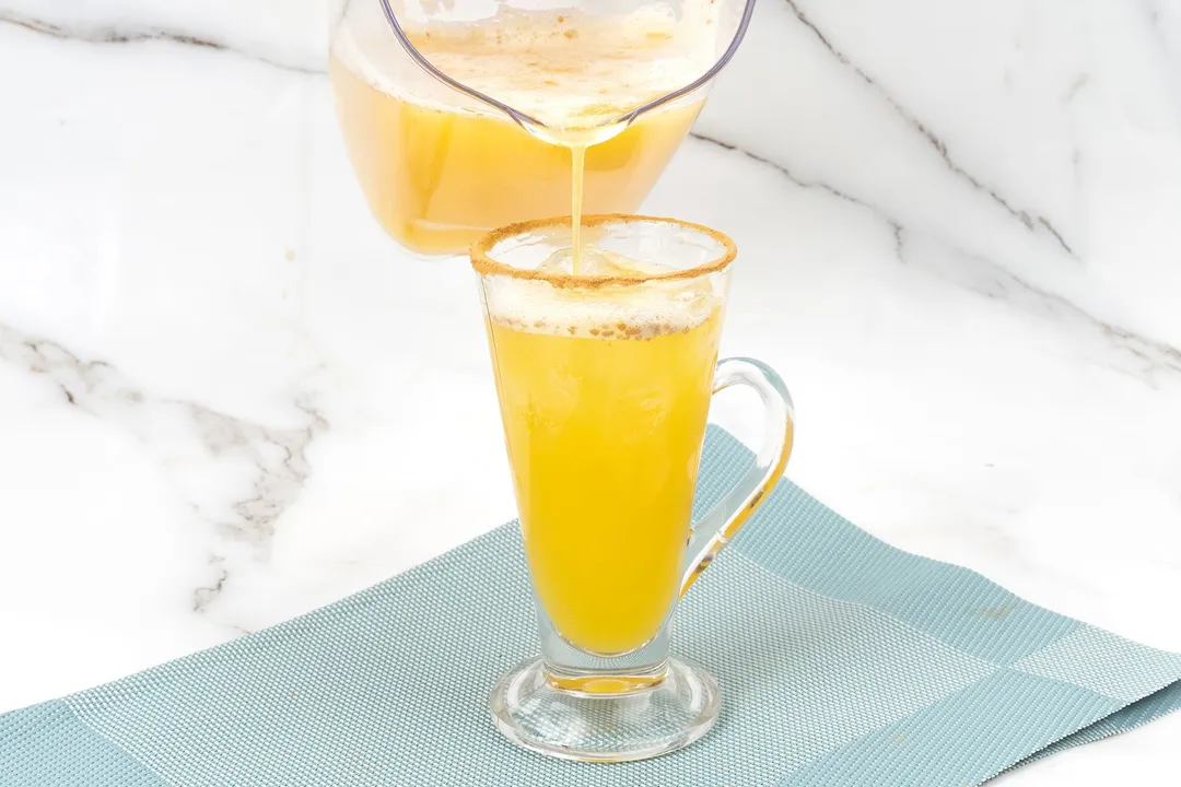 pouring pineapple juice and rum from a pitcher to a glass