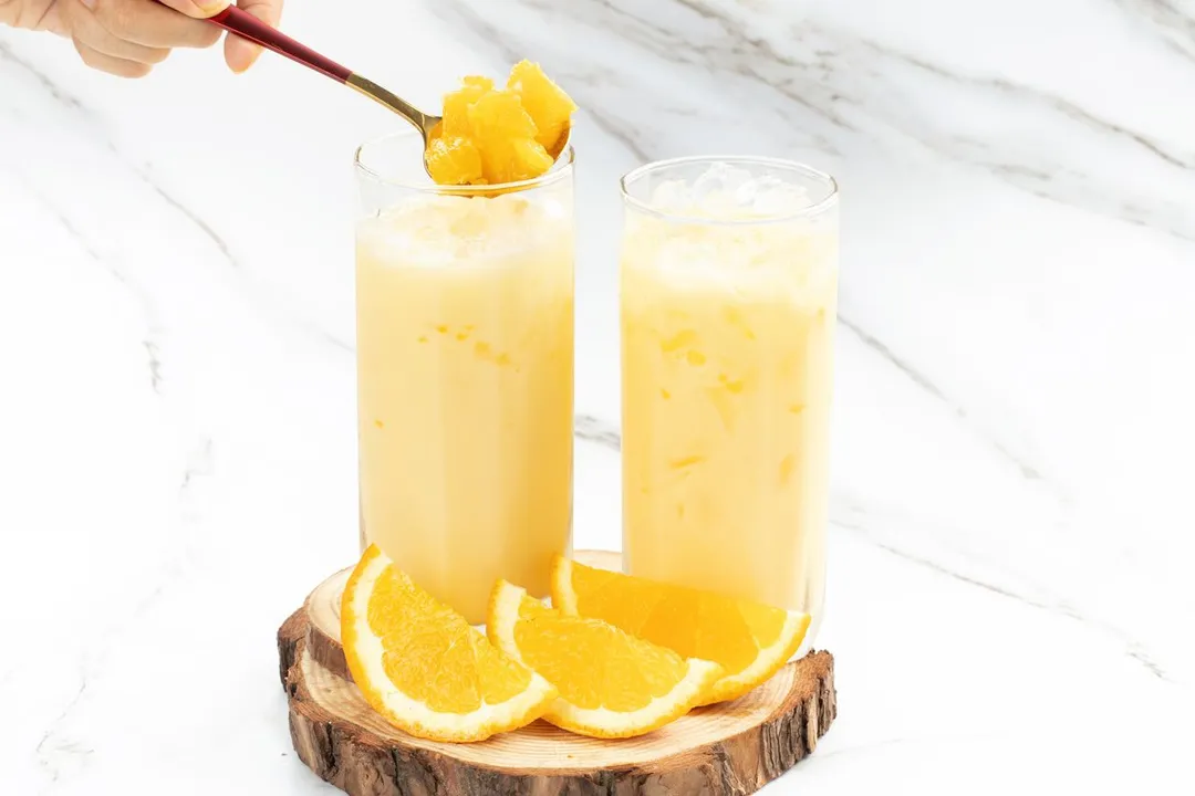 a spoon of fresh orange on top of two glasses of milk and orange juice