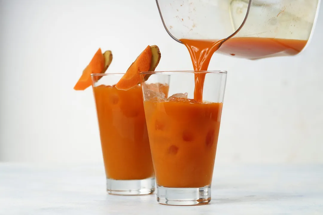 A jug pouring Carrot Ginger Turmeric Juice into a glass.