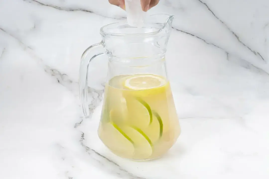 Granulated sugar poured into a clear glass pitcher of ginger lemonade filled with citrus slices