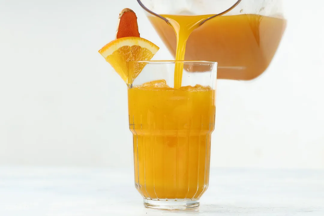 pouring orange turmeric juice from pitcher to a glass