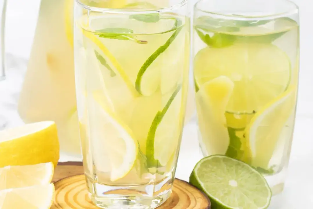 Two glasses of ginger water filled with lemon and lime slices, mints, and put next to extra lemon and limes