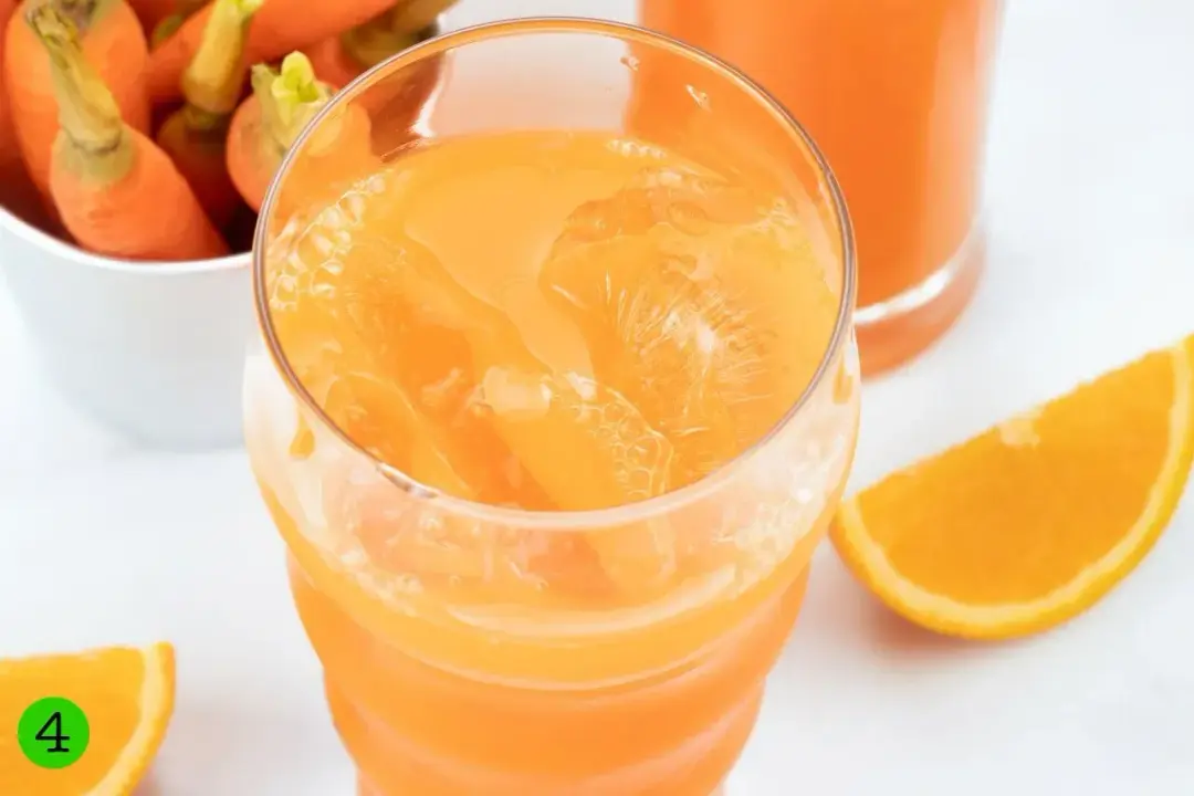 A tall glass of orange carrot juice garnished with an orange wedge put by the window