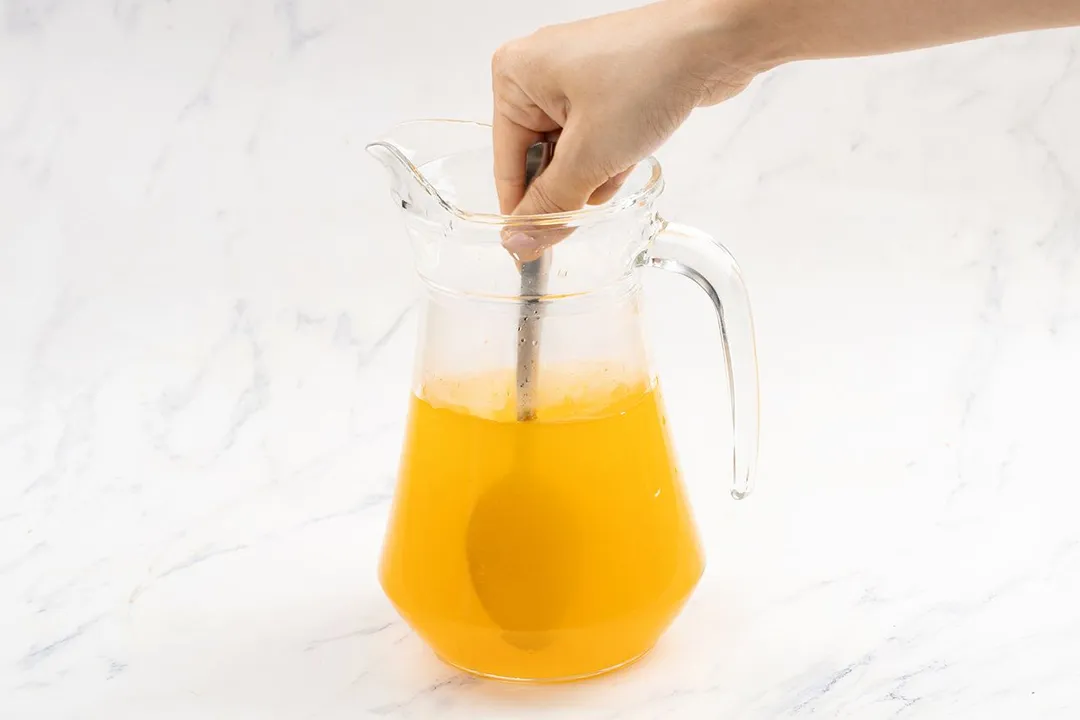 a hand holding a spoon whisk turmeric and apple cider vinegar on a pitcher