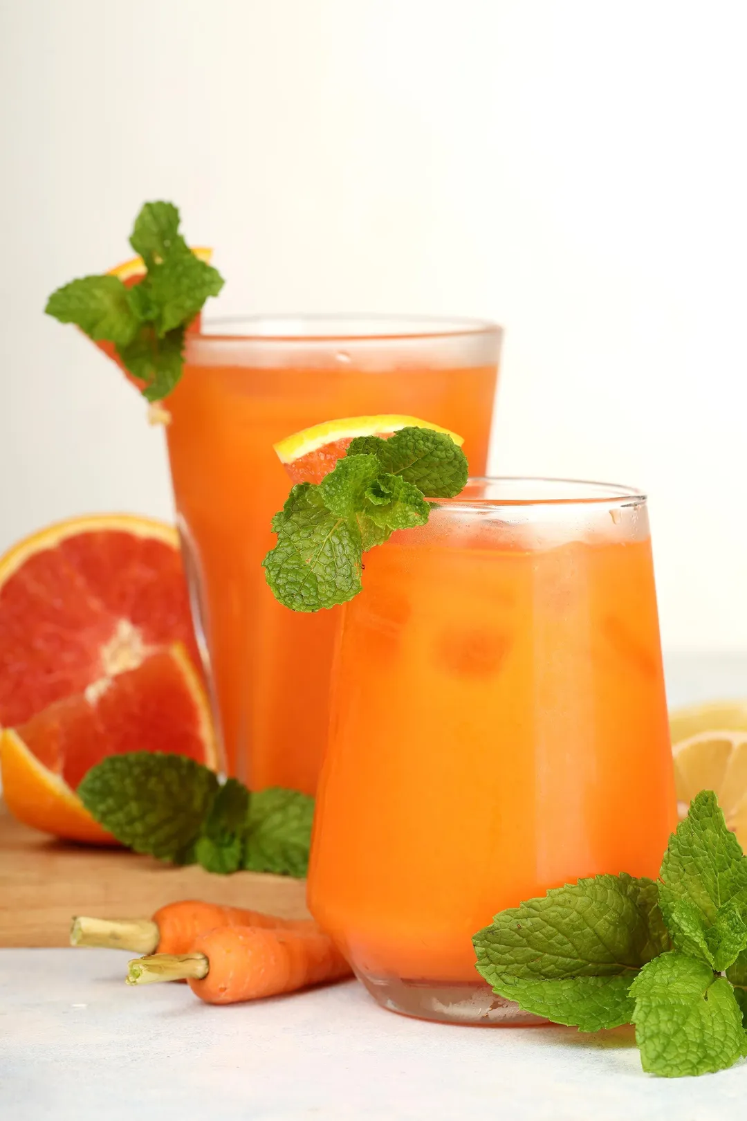 two glasses of grapefruit carrot juice decorated with carrot mint leaves and half grapefruit