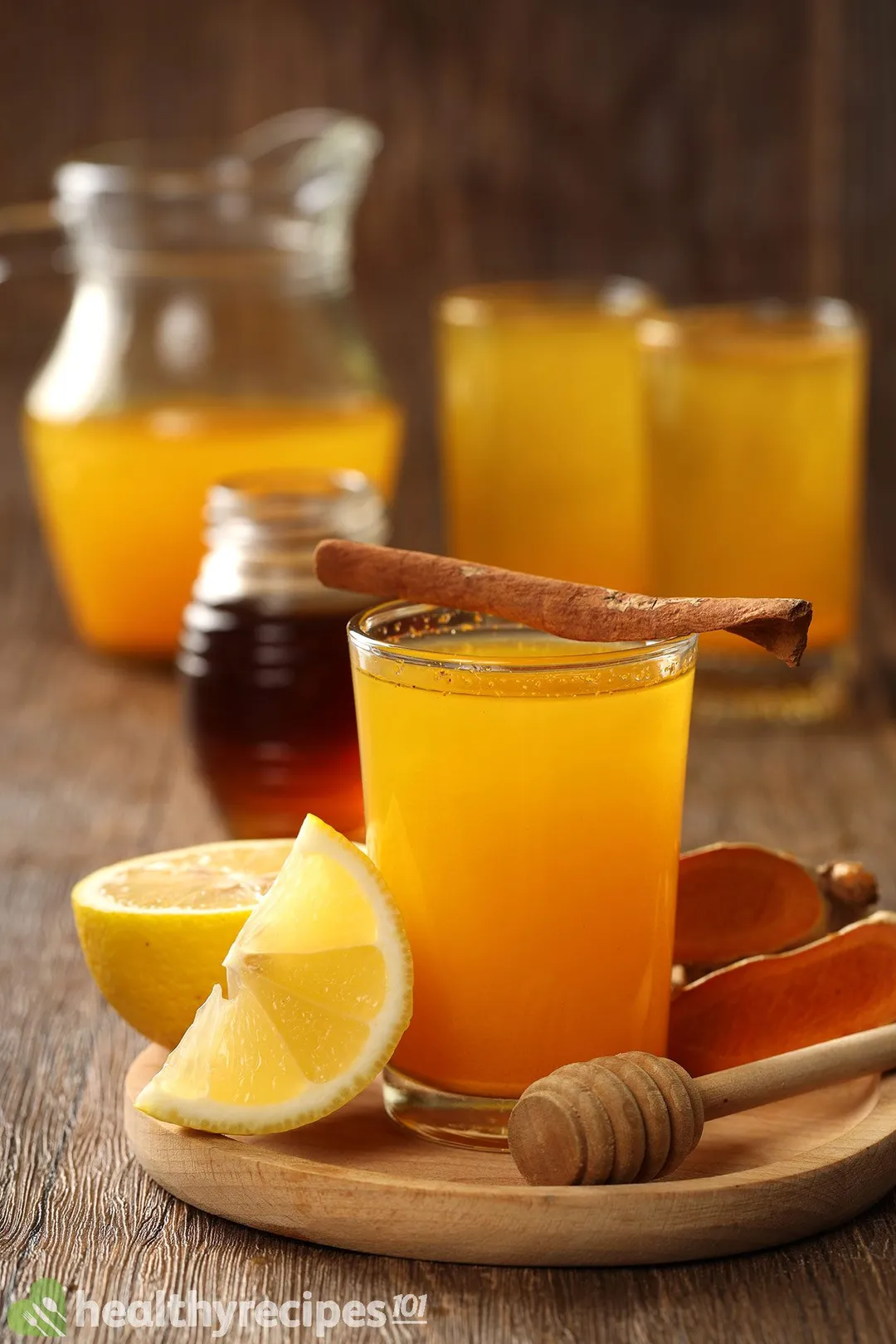 a glass of turmeric and lemon juice on a tray decorated with honey jar and lemon wedge