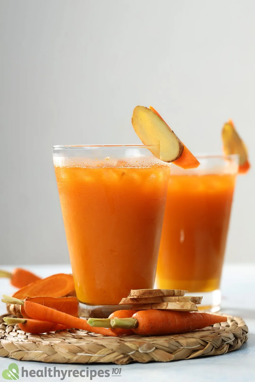 Two glasses of Carrot Ginger Turmeric Juice placed near baby carrots and ginger slices.