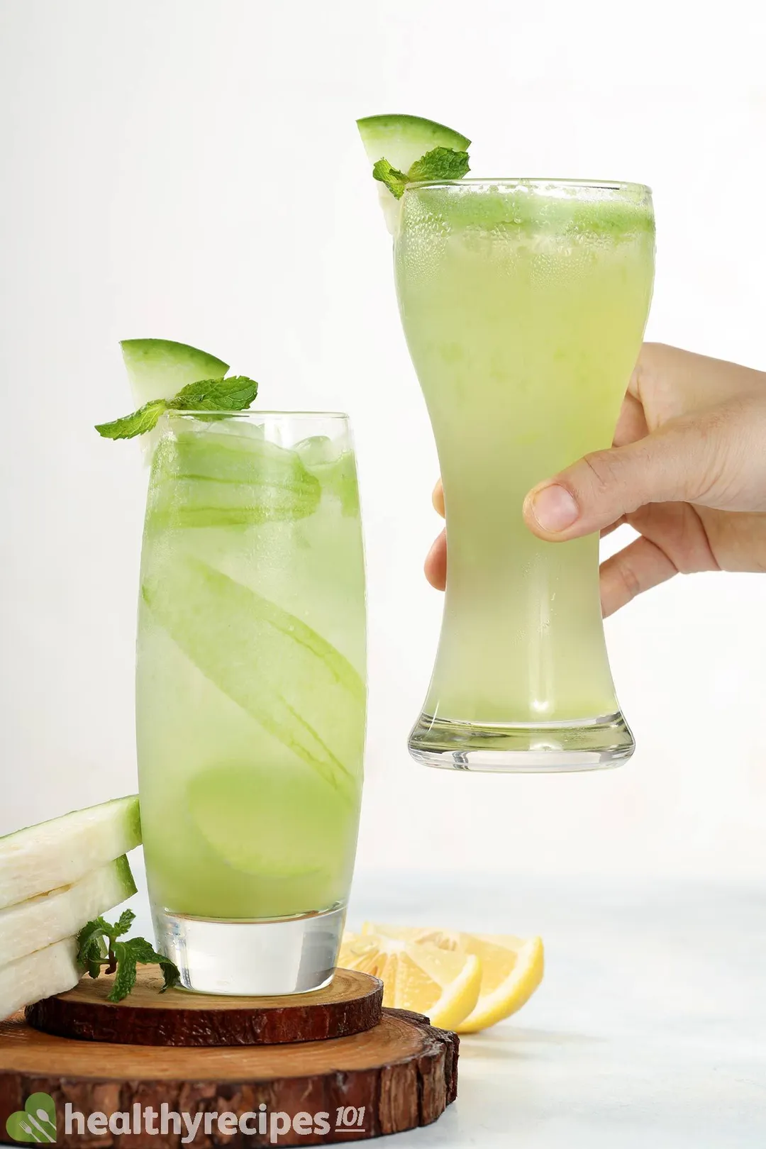 A hand picking up a tall glass of winter melon juice. There's another winter melon juice next to it placed on a wooden coaster.