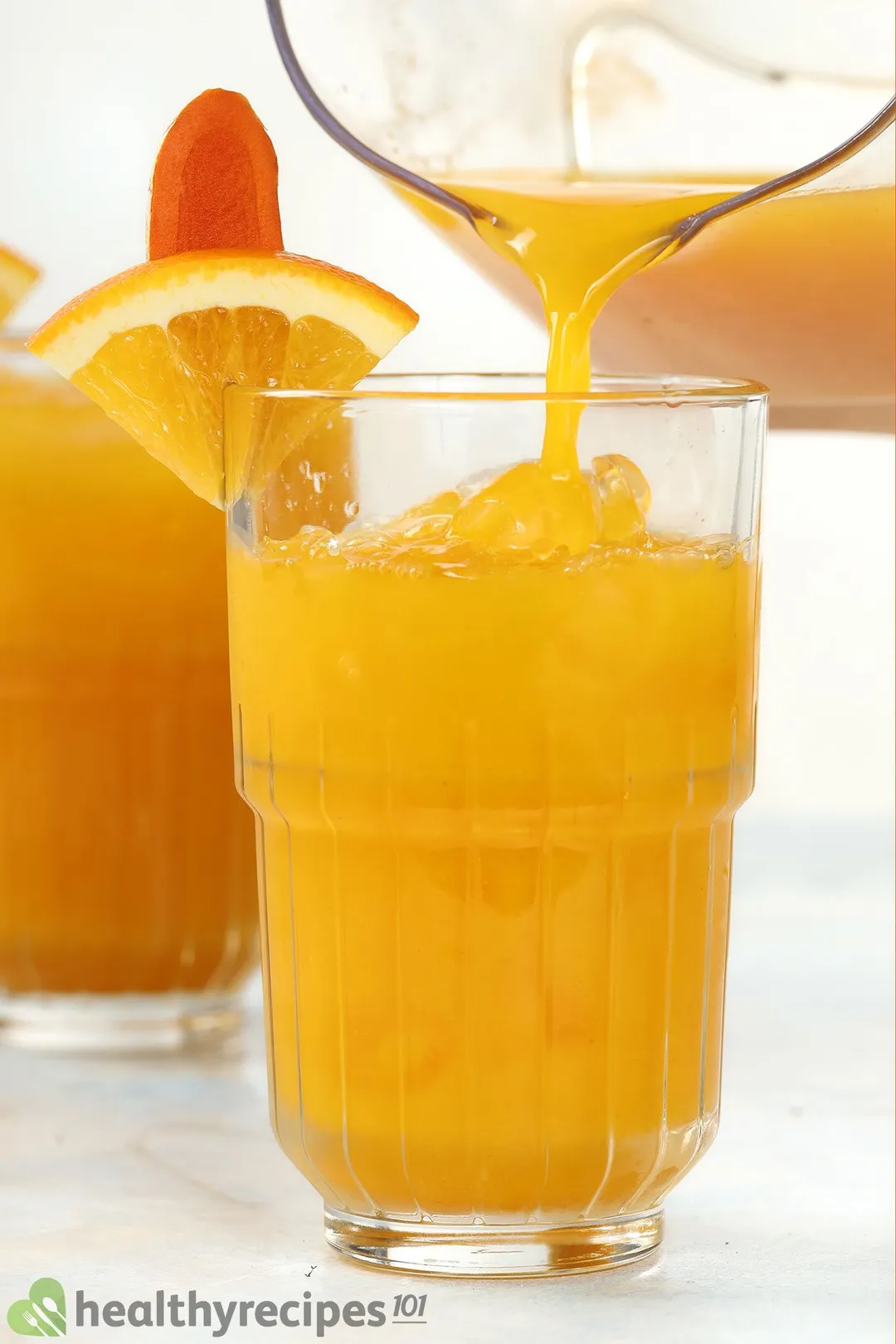 pouring orange turmeric juice from a pitcher into a glass