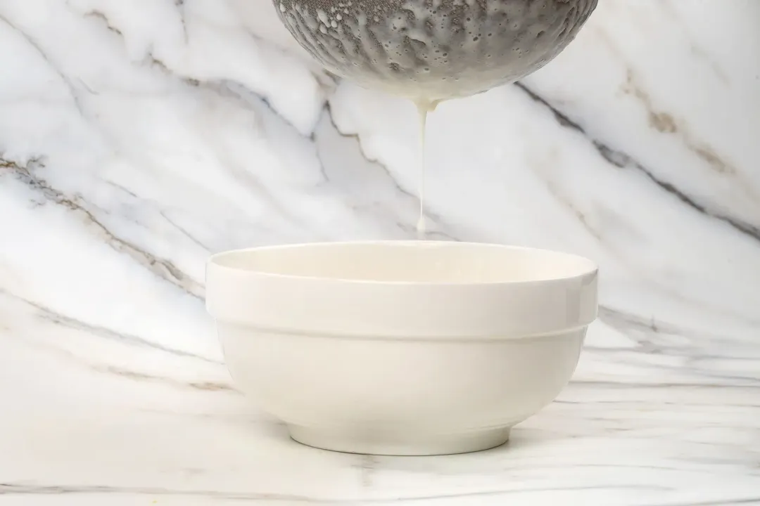 Soursop juice running through a sieve from the top down into a white bowl