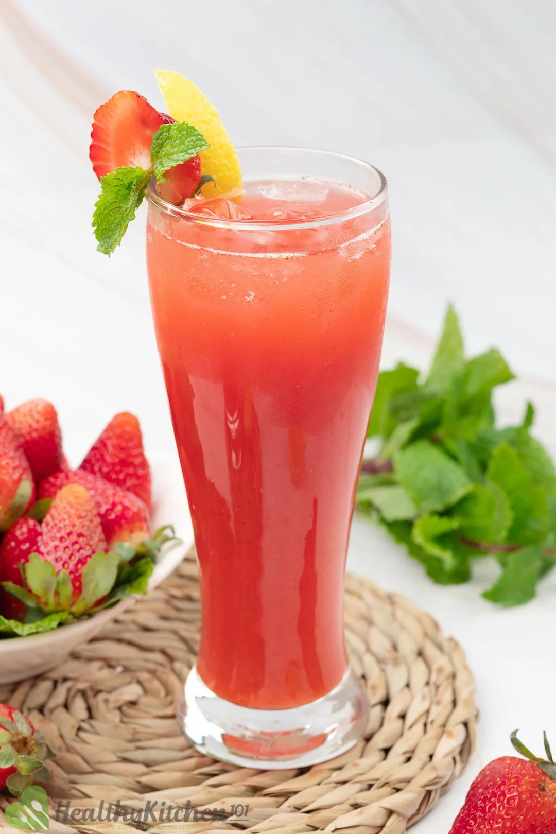 a glass of Strawberry Juice surrounded by a plate of strawberry mint leaves