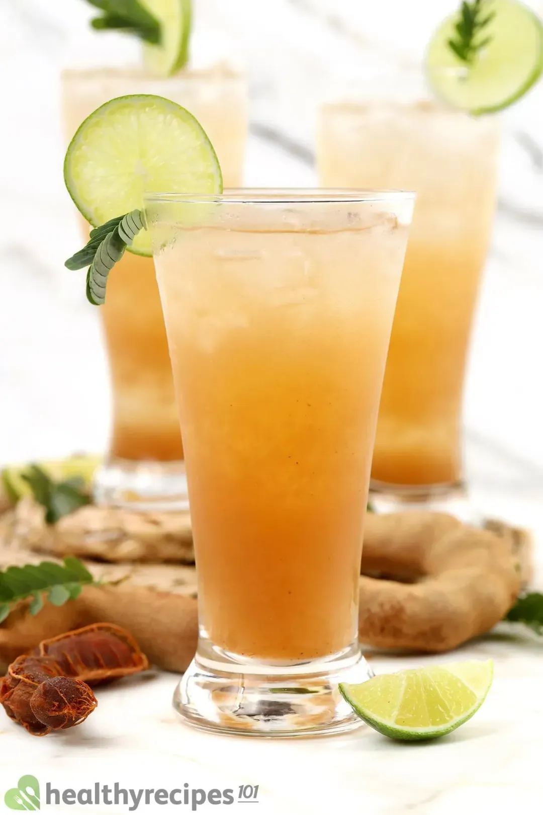 Three iced tamarind drinks with lemon wheels on their brims, put next to garnishes