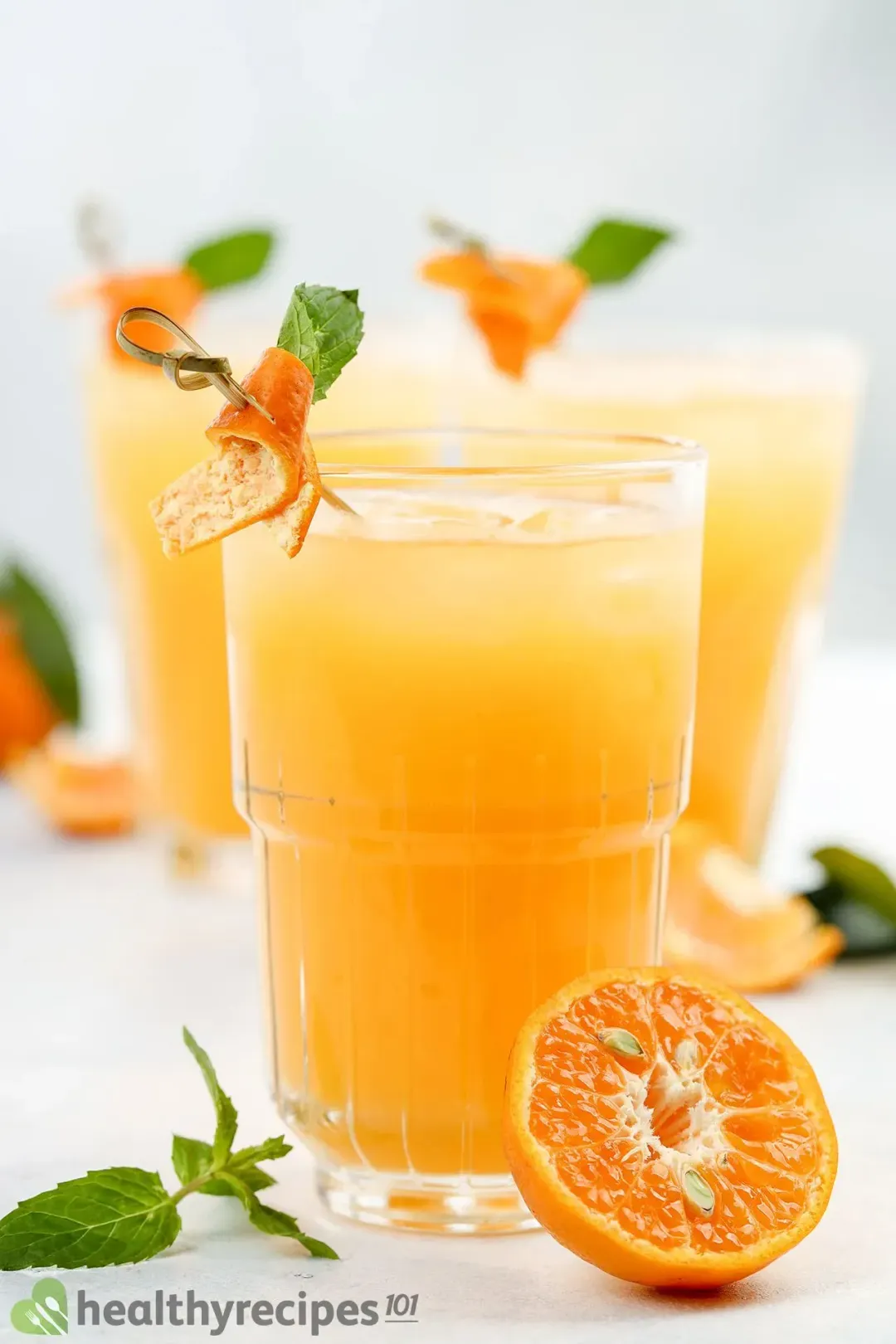 a glass of Tangerine Juice decorated with half Tangerine fruit and mint leaf, two glasses in background