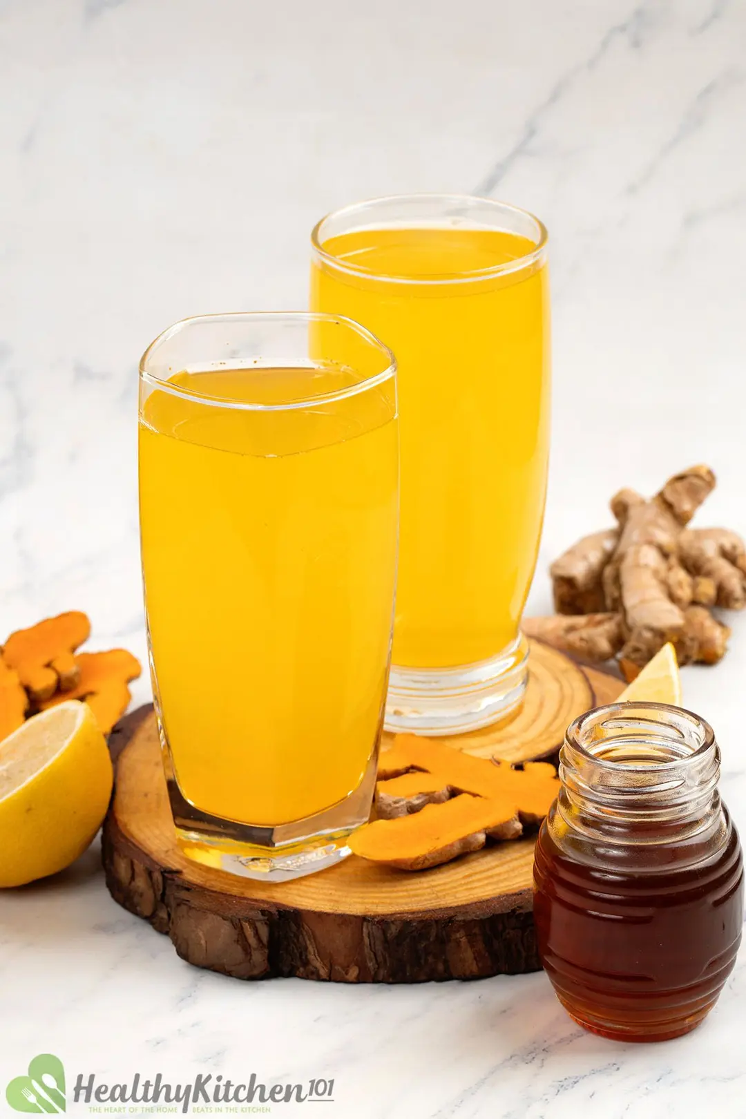two glasses of turmeric and acv put side by side garnish with honey jar, turmeric and half lemon