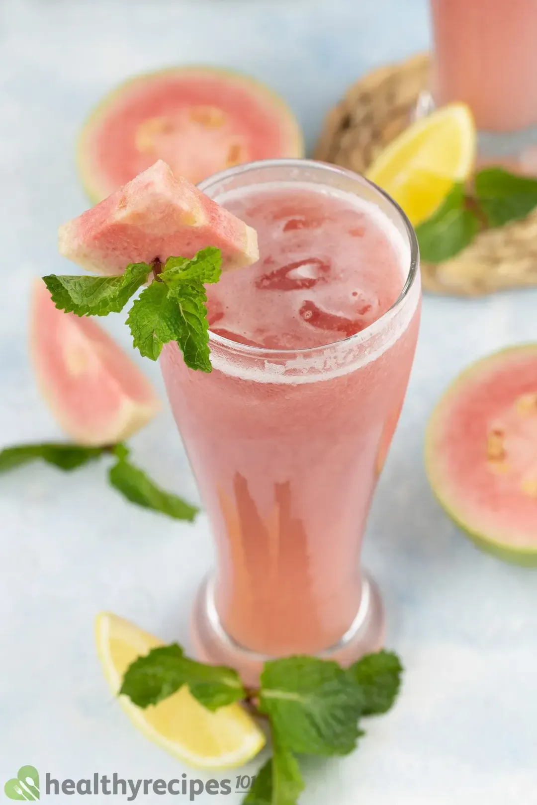 A high-angle shot of a glass of guava juice, guava slices, mint leaves, and a lemon wedge