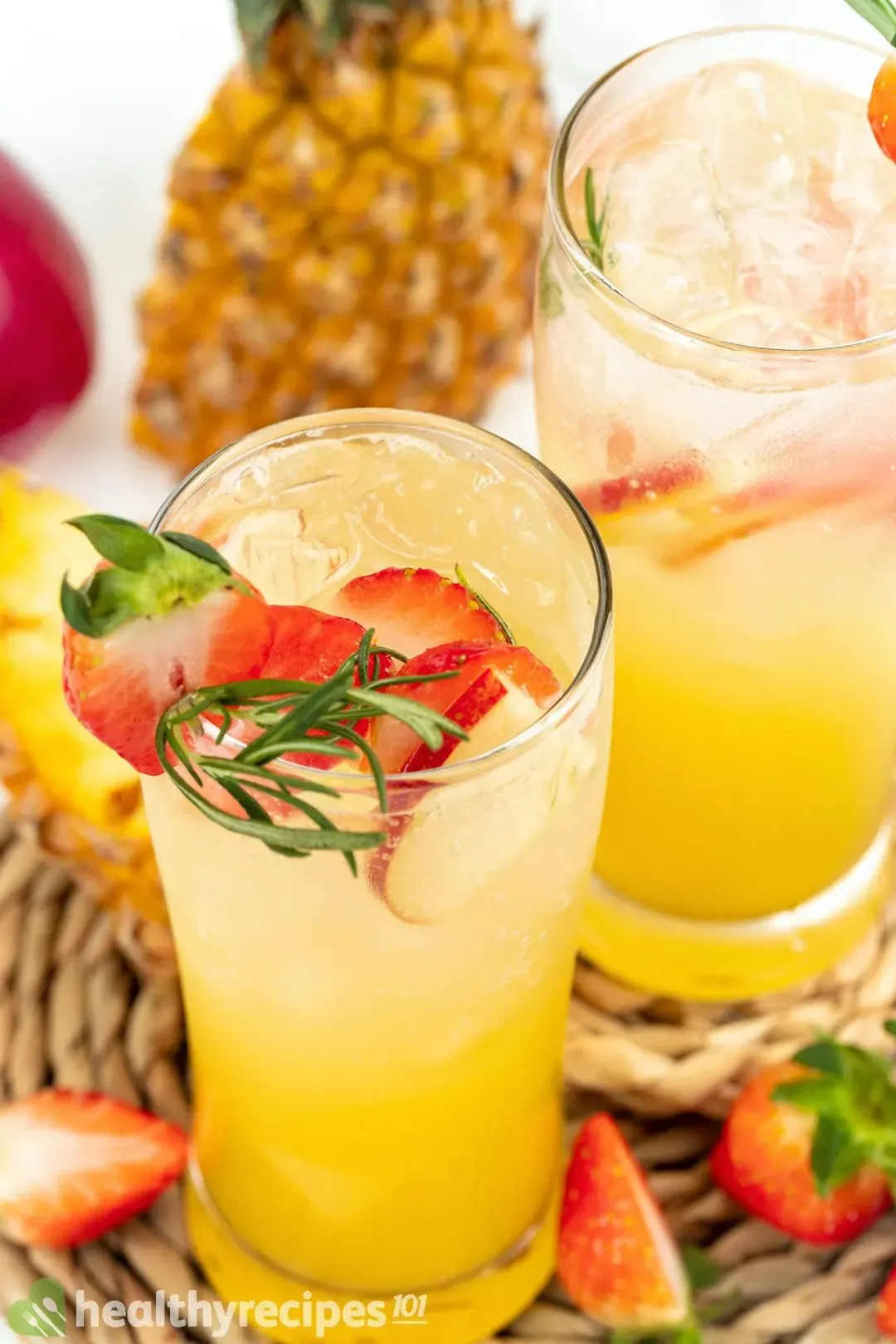 A shot from the top of two orange jungle juice cocktail, topped with rosemary and strawberry slices