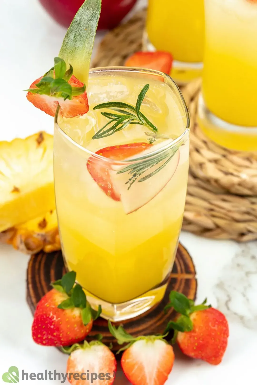 An iced glass of orange jungle juice with strawberries and rosemary as garnish