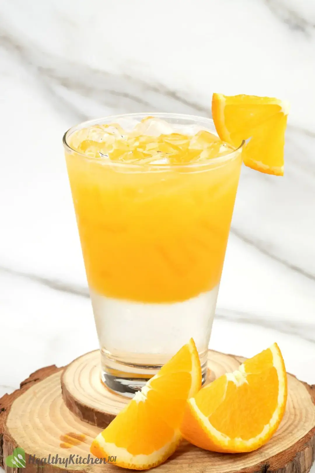 A glass of orange juice vodka and sugar syrup separated in two layers, garnished with orange wedges