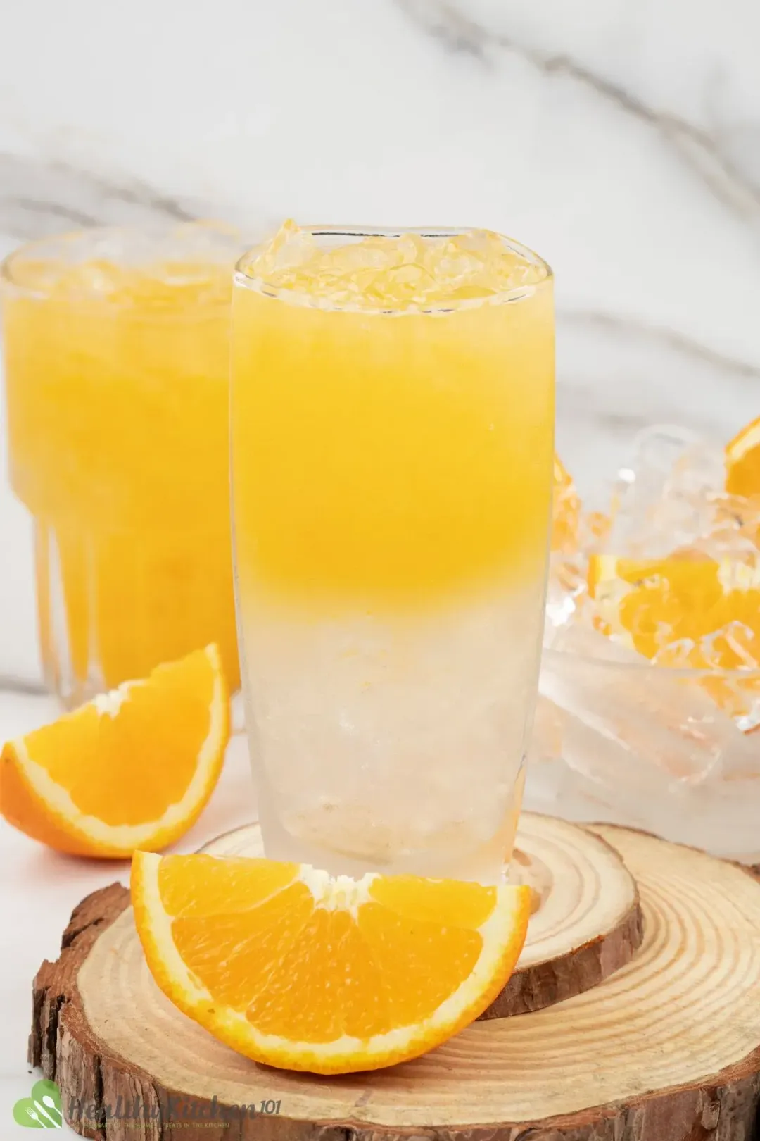 A glass of orange juice, vodka, and sugar syrup in 2 layers, next to orange wedges and an orange juice glass