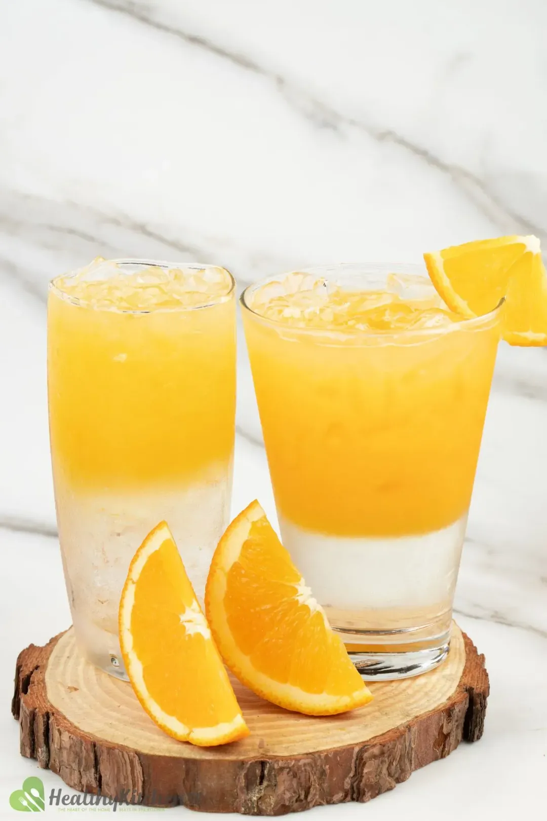 Two glasses of orange juice and vodka separated in two layers, garnished with orange wedges