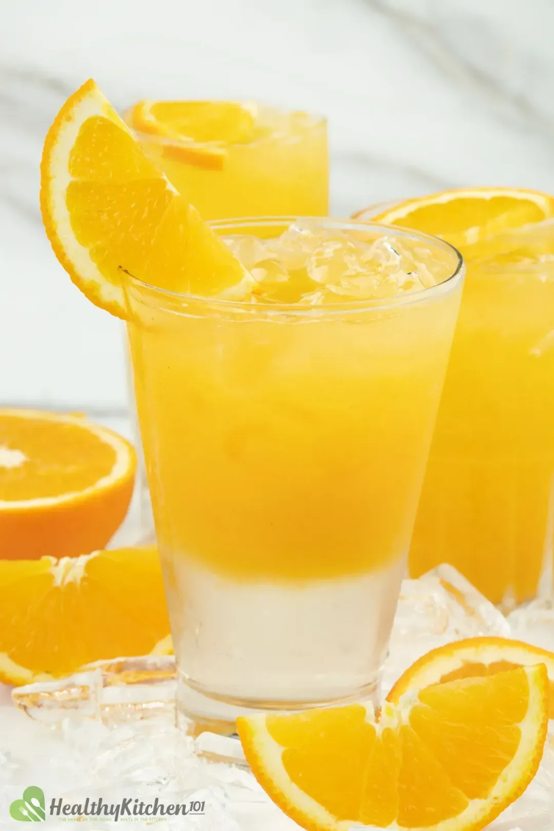 A glass of orange juice on top and sugar syrup layer at the bottom, next to orange wedges and an orange juice glass