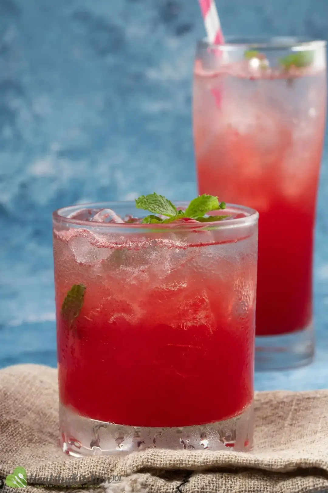 A small and round glass of watermelon juice filled with ice and garnished with several mint leaves