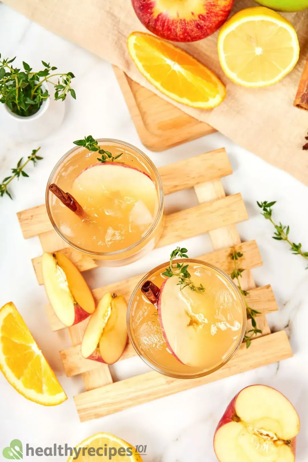 A picture taken from the top of two apple cider cocktail garnished with rosemary sprigs, apple wedges, oranges, and cinnamon sticks