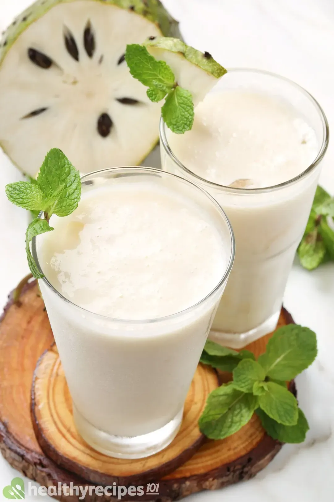 Two iced glasses of soursop juice, garnished with mints around and a cut-open soursop in the back
