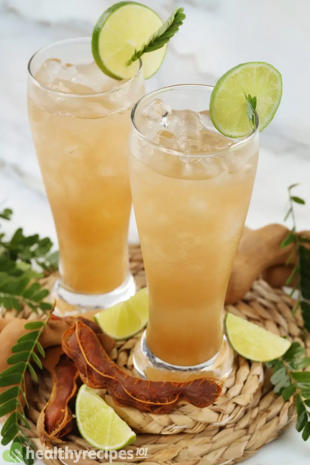 Two glasses of iced tamarind juice, garnished with lime wheels on the brim and peeled tamarinds on the side