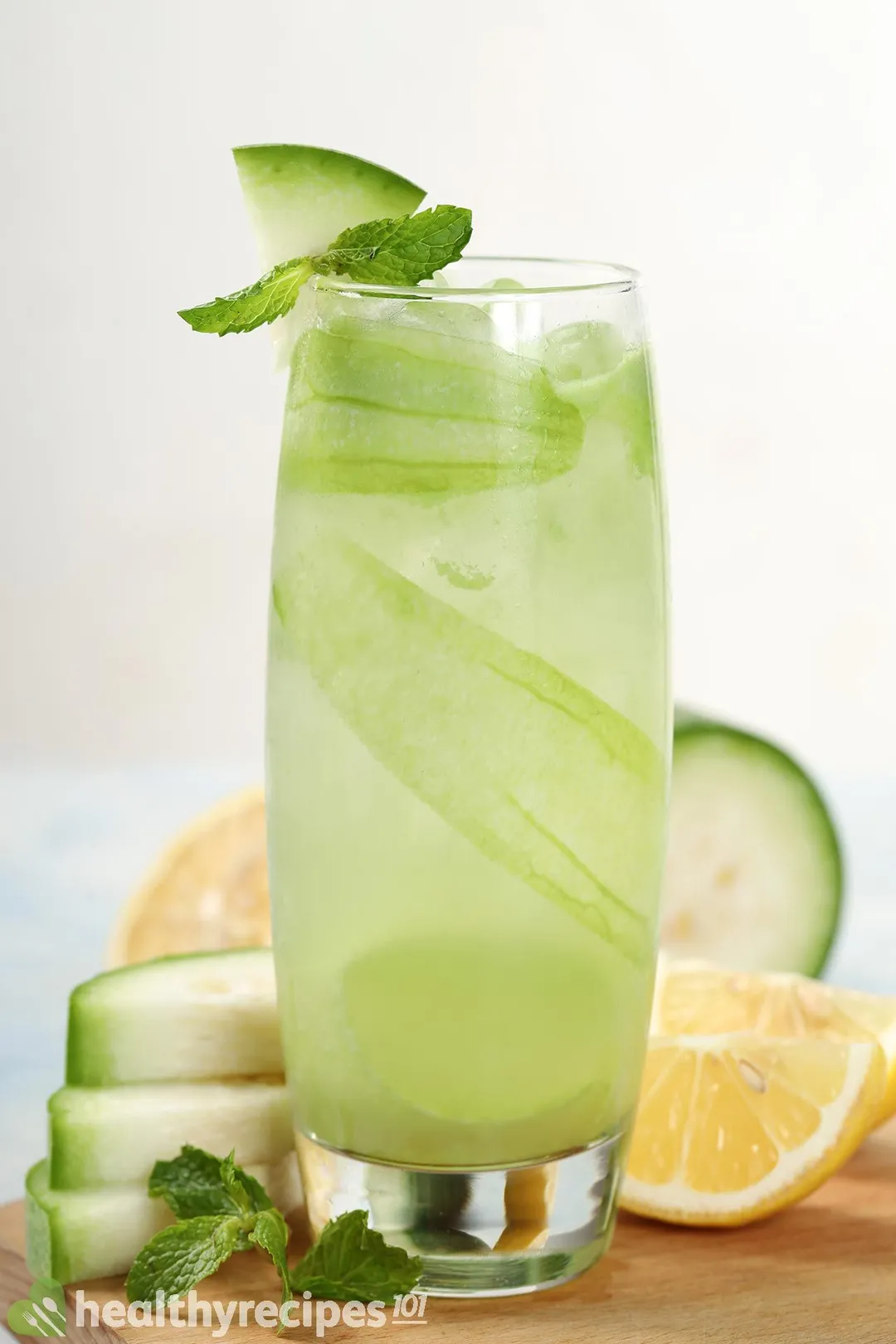 A tall glass of winter melon juice placed on a wooden board near lime wedges and winter melon slices.