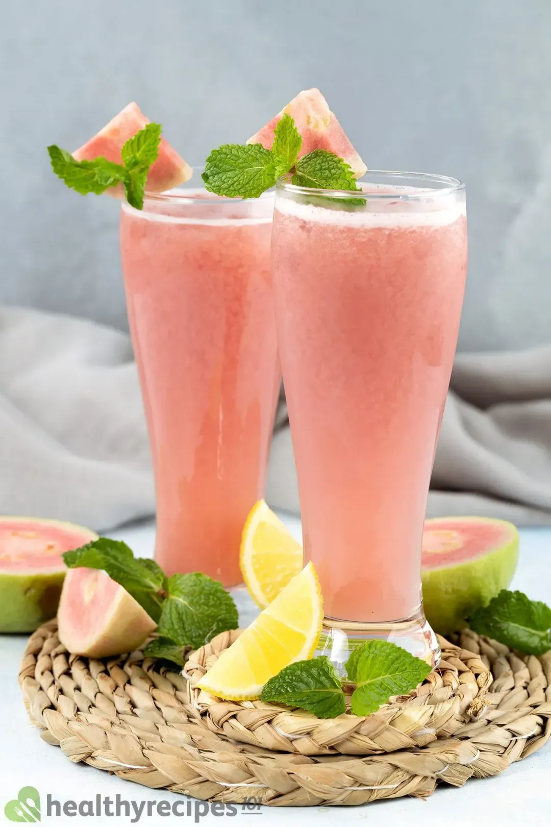 Two tall and pink glasses of guava juice surrounded by lemon wedges and large guava slices
