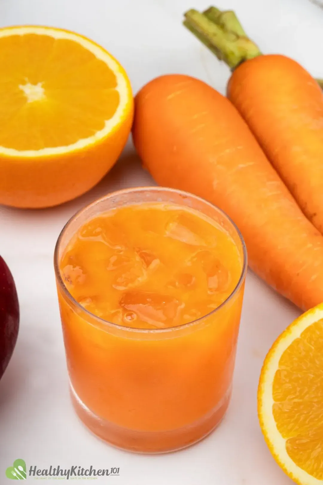 An iced glass of carrot drink next to orange halves and whole carrots