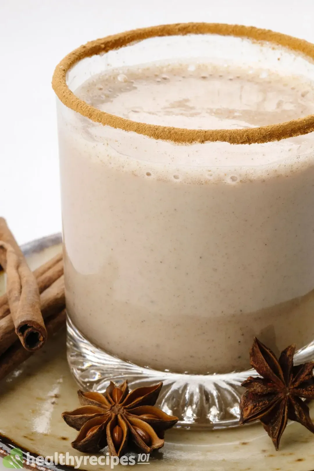 A short glass of foamy eggnog with cinnamon sticks and star anise