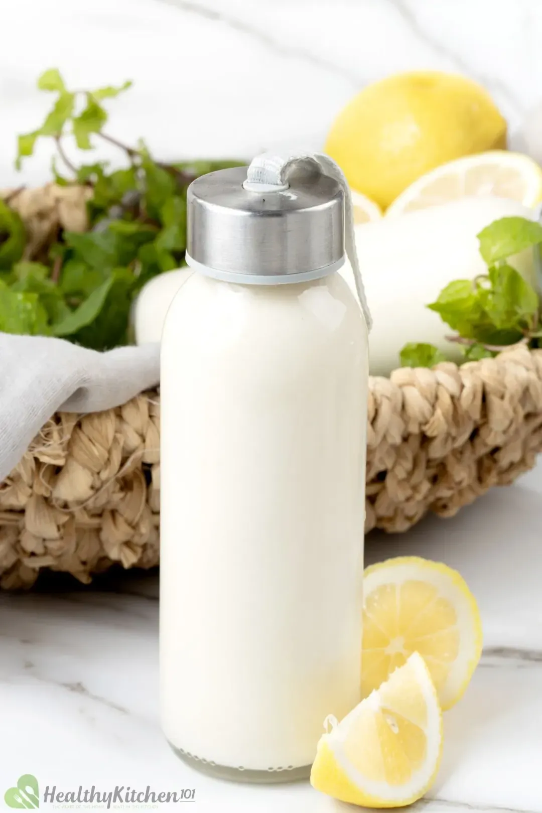 A bottle of milk put next to some lemon wedges in front of a basket of mints