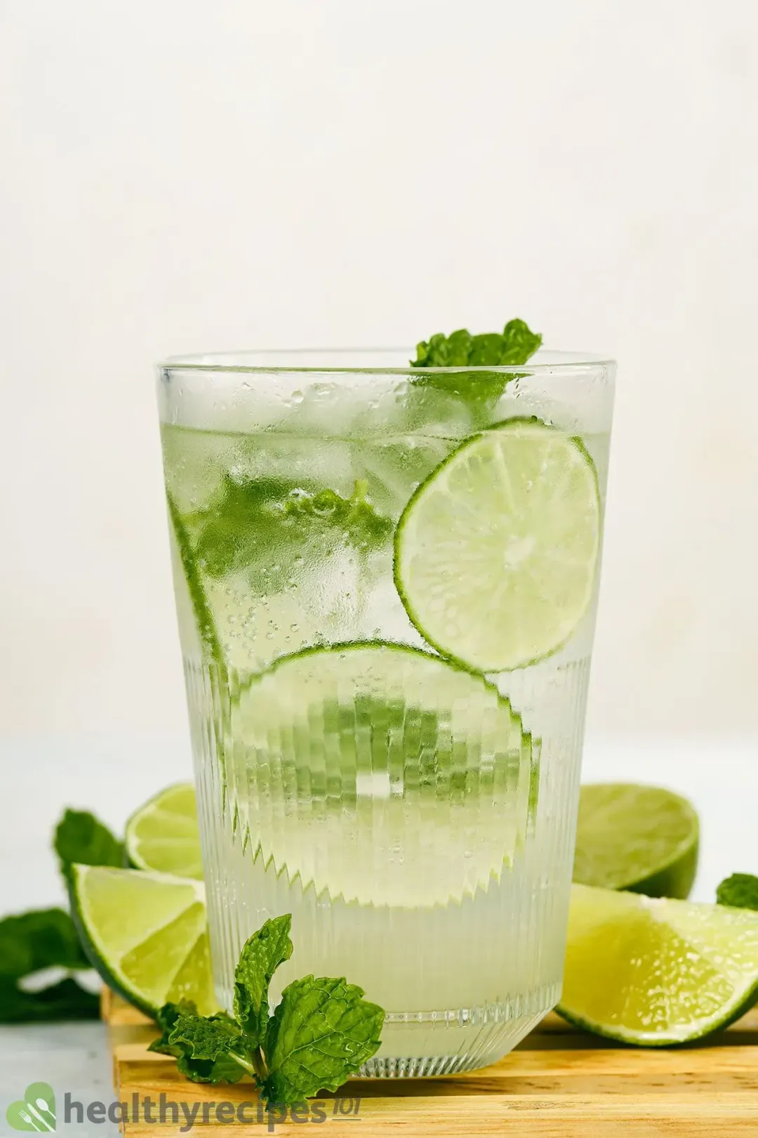 An iced glass of mojitos, garnished with lots of lime wedges and mint leaves