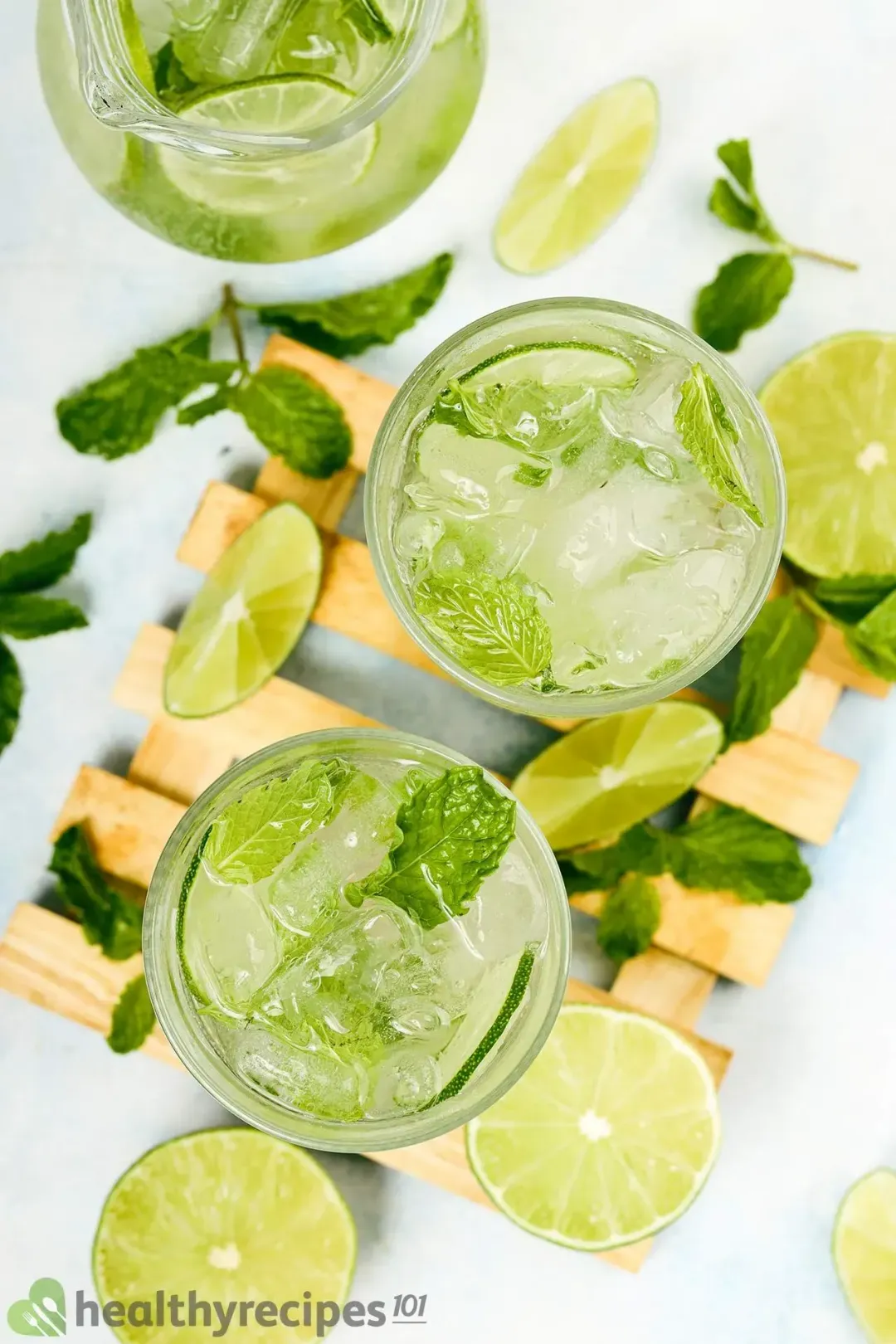 A shot from the top of three mojito glasses, with mint leaves and lime wedges lying round