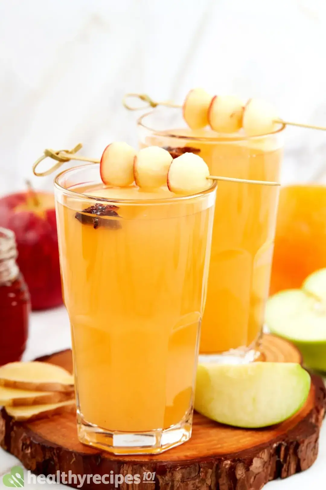 Two tall glasses filled to the top with hot toddy cocktail, garnished with star anise, apple ball skewers, and apple wedges